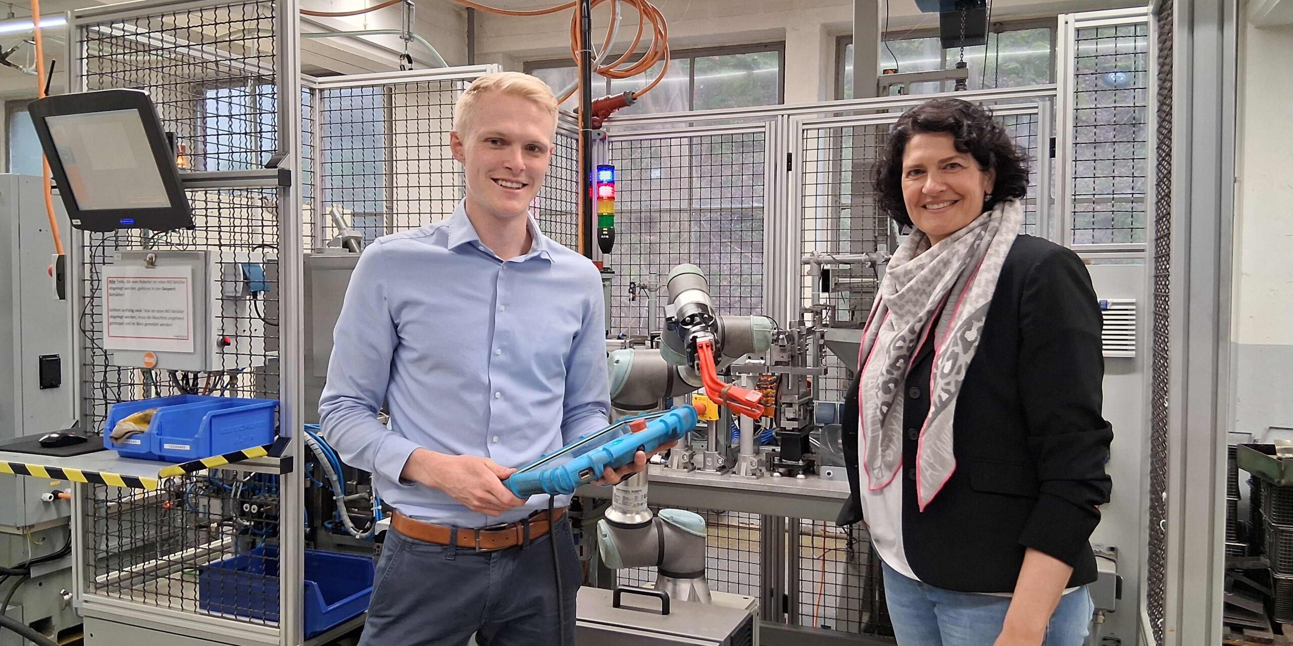 Zwei Personen stehen vor einem Roboter und halten ein Tablet in der Hand.