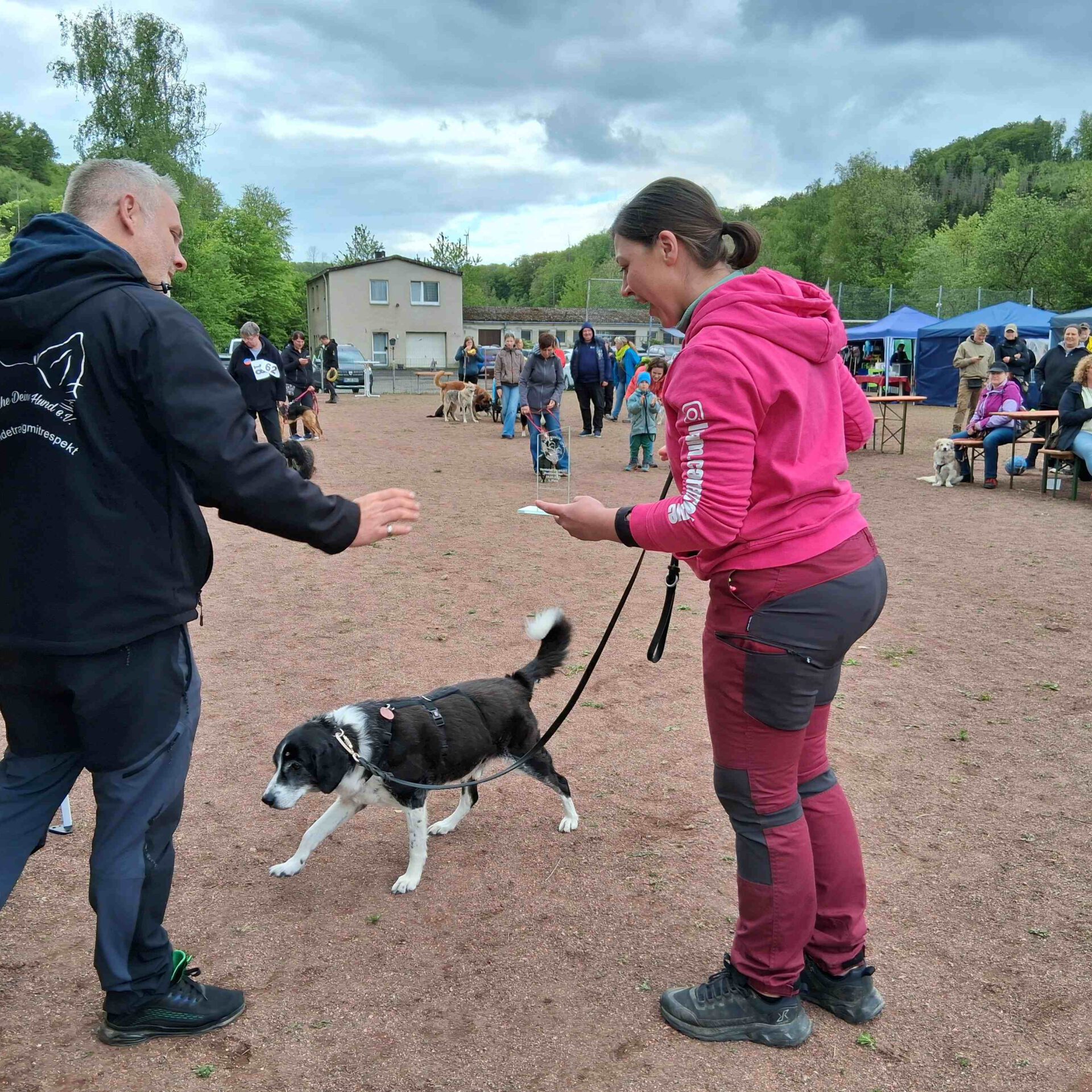 Eine Frau mit ihrem Hund beim Hunderennen. Im Hintergrund schauen die Zuschauer.