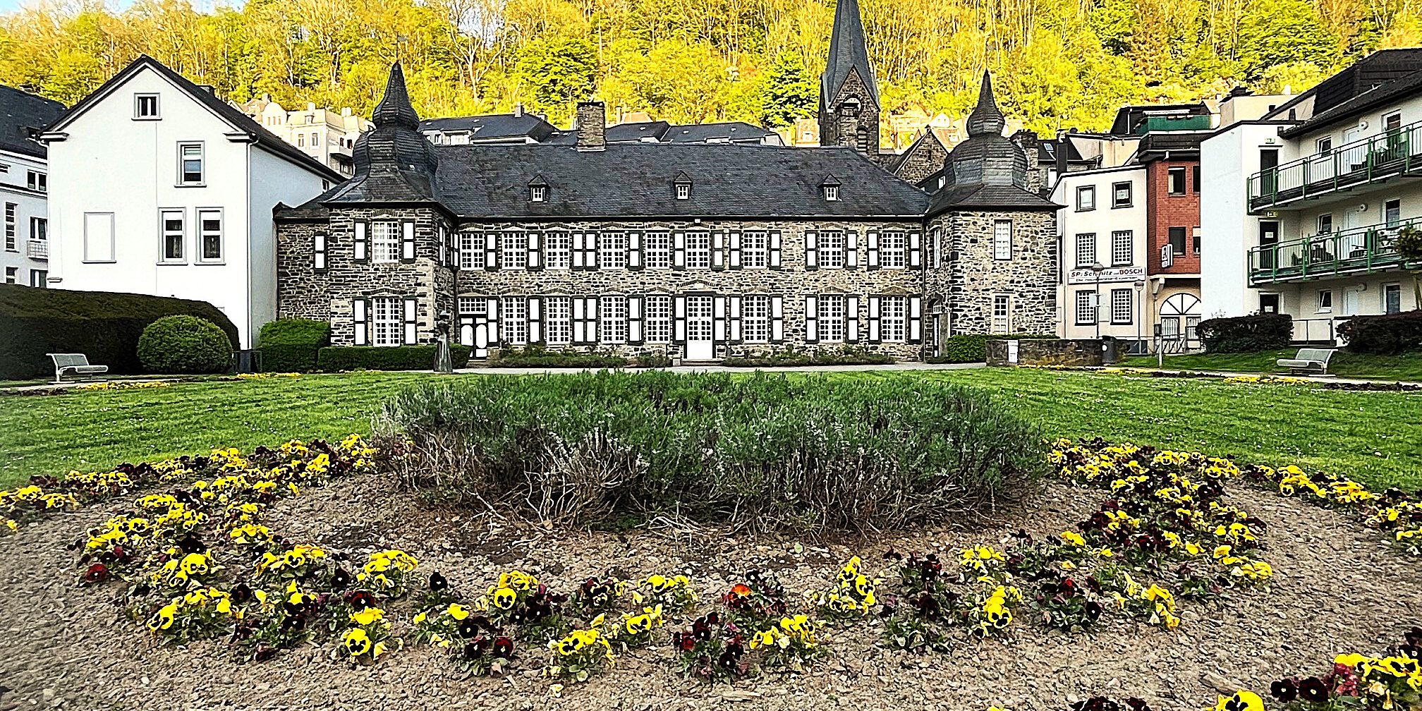 Wie bewerten die Menschen das Leben in Altena, Nachrodt-Wiblingwerde und Umgebung? Machen Sie bei unserer Umfrage mit!
© Archiv-Foto: Carsten Menzel In einer parkähnlichen Gartenanlage blühen dunkelrote und gelbe Stiefmütterchen vor einem burgähnlichen Anwesen.