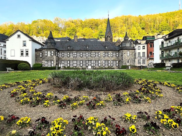 Archiv-Foto: Carsten Menzel In einer parkähnlichen Gartenanlage blühen dunkelrote und gelbe Stiefmütterchen vor einem burgähnlichen Anwesen.