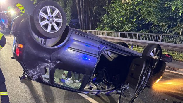 Foto: P. Selle/Feuerwehr Altena Ein blauer Kleinwagen liegt in der Dunkelheit mitten auf einer Straße auf dem Dach.