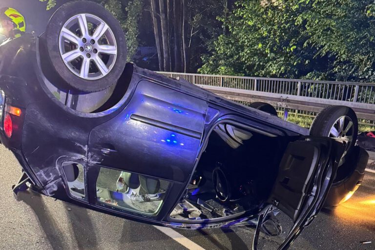Ein blauer Kleinwagen liegt in der Dunkelheit mitten auf einer Straße auf dem Dach.