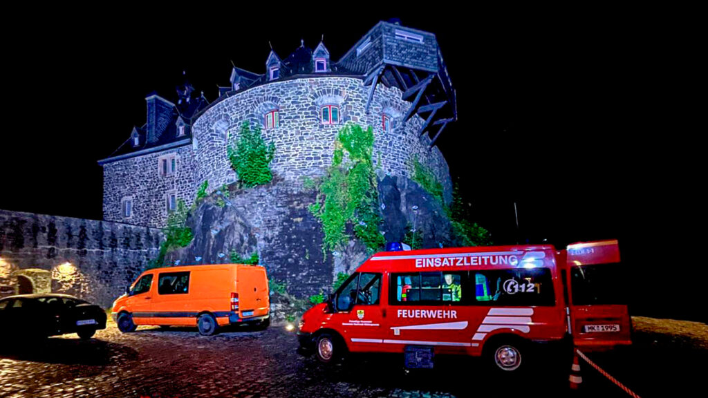 Ein Einsatzleitwagen der Feuerwehr steht bei Nacht auf einem Parkplatz der beleuchteten Burg Altena.