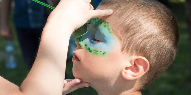 Ein Junge wird im Gesicht bunt geschminkt.