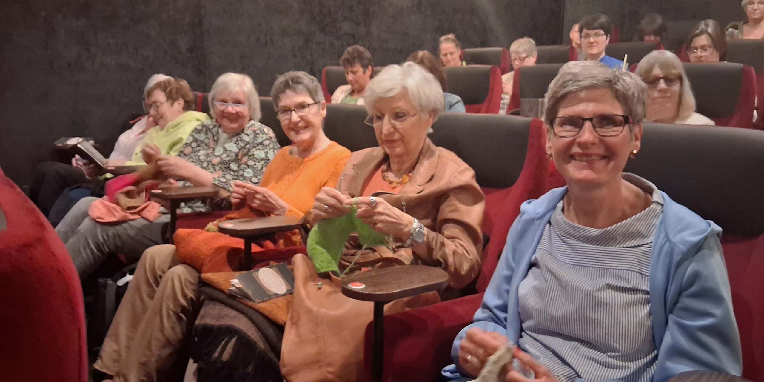 Mehrere Frauen sitzen in einem dunklen Kinosaal und stricken während einer Filmvorstellung.