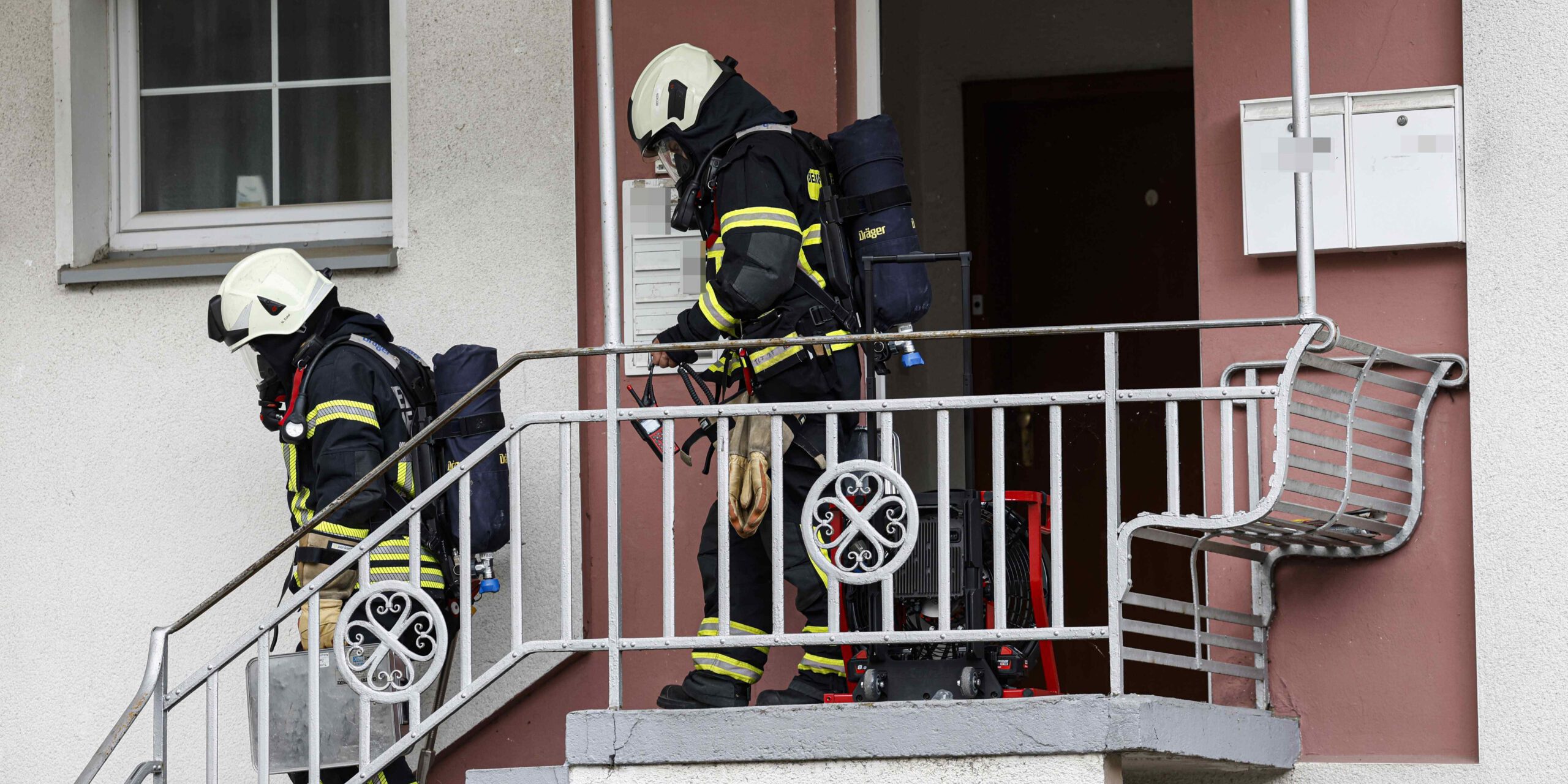 Zwei Feuerwehrleute mit Atemschutz verlassen ein Haus über eine Außentreppe