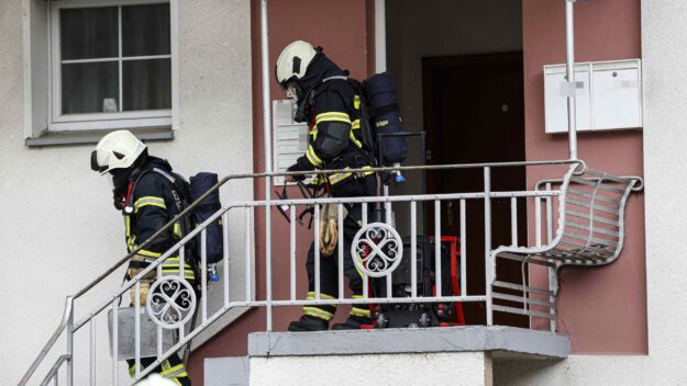 Zwei Feuerwehrleute mit Atemschutz verlassen ein Haus über eine Außentreppe