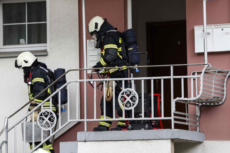 Zwei Feuerwehrleute mit Atemschutz verlassen ein Haus über eine Außentreppe