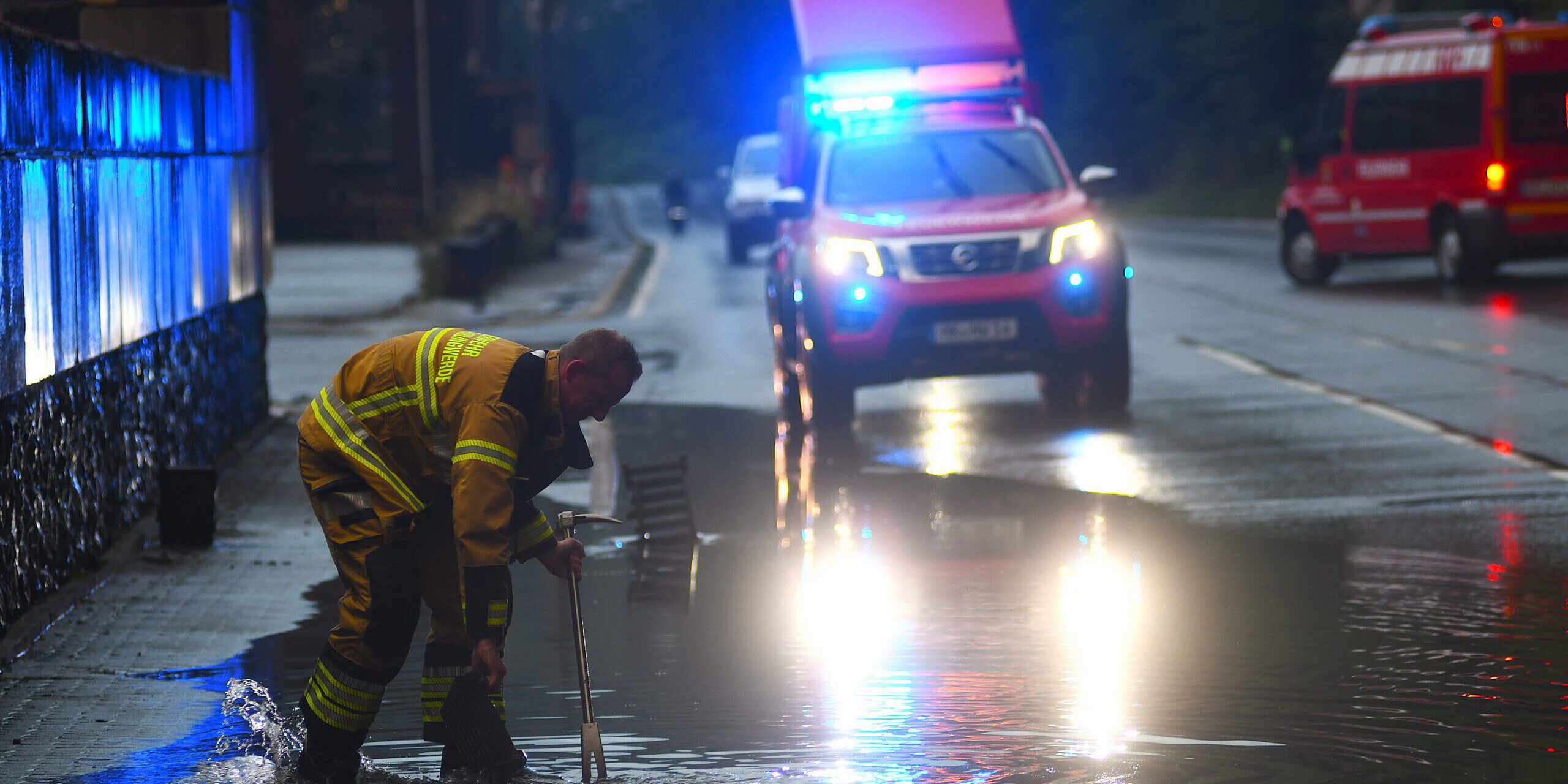 Ein Feuerwehrmann sucht mit einem Halligantool in einer Wasserlache nach einem Gully.