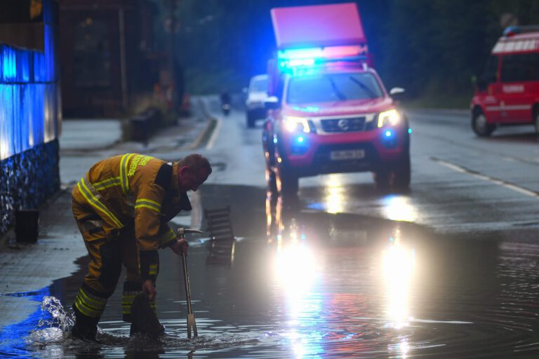 Ein Feuerwehrmann sucht mit einem Halligantool in einer Wasserlache nach einem Gully.