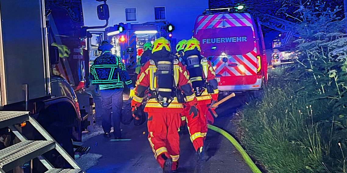 Feuerwehrmänner unter Atemschutz gehen zwischen Einsatzfahrzeugen auf ein Reihenhaus zu.