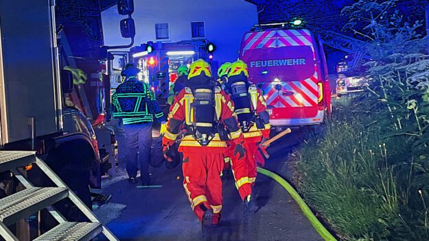 Foto: Carsten Menzel Feuerwehrmänner unter Atemschutz gehen zwischen Einsatzfahrzeugen auf ein Reihenhaus zu.