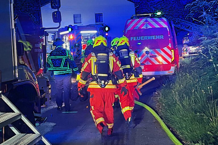 Feuerwehrmänner unter Atemschutz gehen zwischen Einsatzfahrzeugen auf ein Reihenhaus zu.