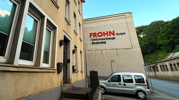 Foto: Carsten Menzel Vor einem beigen Industriegebäude parkt ein silbernes Firmenfahrzeug. Im Hintergrund verläuft eine Straße.