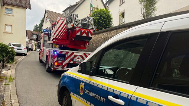 Foto: Carsten Menzel Ein Drehleiterfahrzeug der Feuerwehr und ein Wagen des städtischen Ordnungsamts stehen hintereinander in einer engen, bergauf führenden Straße, rechts und links dichte Bebauung durch Wohnhäuser.