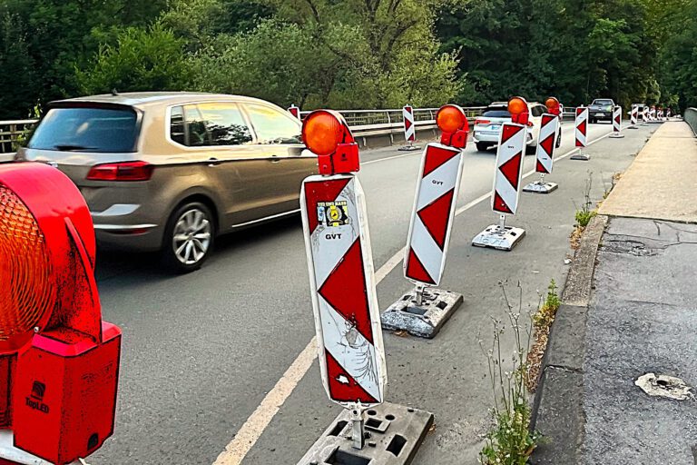 Die Fahrbahn auf einer Brücke ist mit rot-weißen Baken auf eine Fahrspur in der Mitte verengt, über die Autos in Richtung Norden fahren