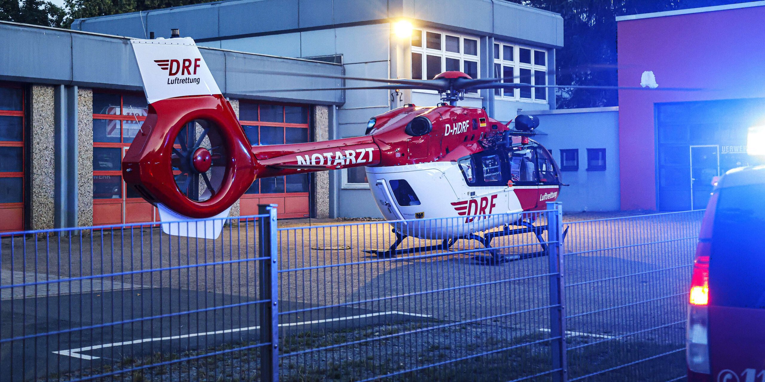 Der Rettungshubschrauber  Ein rot-weißer Rettungshubschrauber steht in der Morgendämmerung auf einem Platz vor einem Feuerwehrgerätehaus.