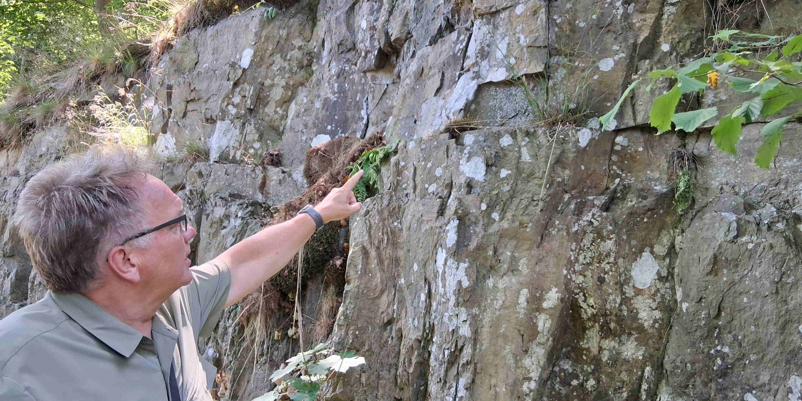Andreas Kisker deutet auf die nach vorne geneigten Spalten im Fels.