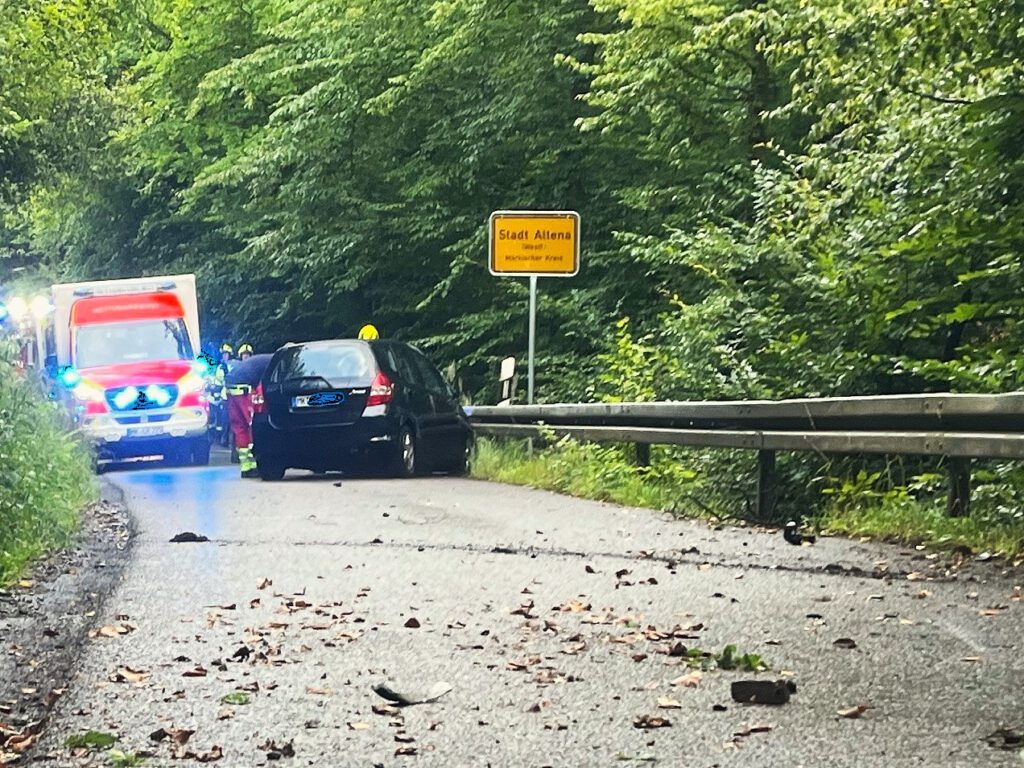 Ein schwarzes Auto steht schräg in einer Leitplanke. Ein Feuerwehrmann beugt sich durch das Seitenfenster ins Innere. Dahinter steht ein Rettungswagen mit eingeschaltetem Blaulicht.