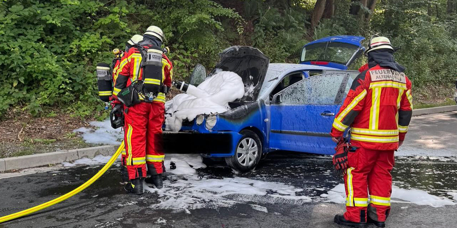 Ein Pkw ist in Altena in Brand geraten. Feuerwehrleute löschen den Motorraum.