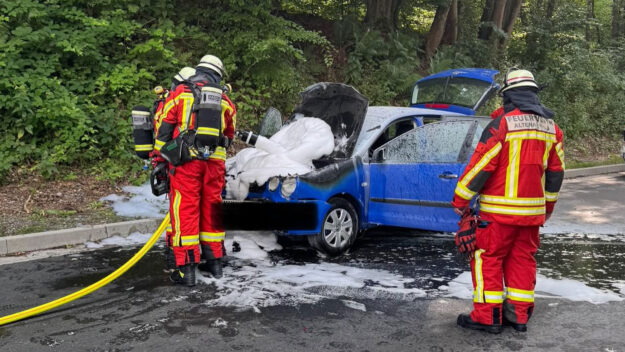 Ein Pkw ist in Altena in Brand geraten. Feuerwehrleute löschen den Motorraum.