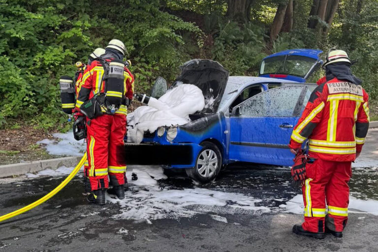 Ein Pkw ist in Altena in Brand geraten. Feuerwehrleute löschen den Motorraum.
