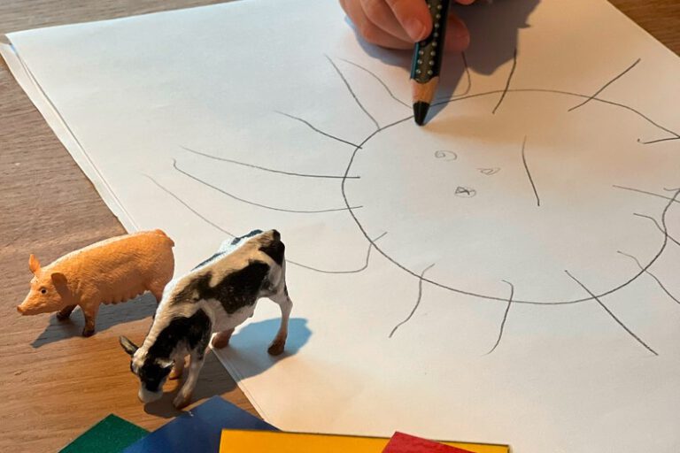 Ein Kind malt eine Sonne auf ein Blatt Papier.