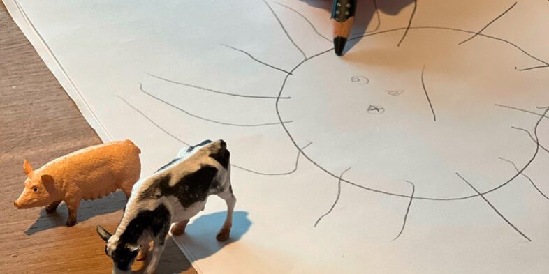 Ein Kind malt eine Sonne auf ein Blatt Papier.