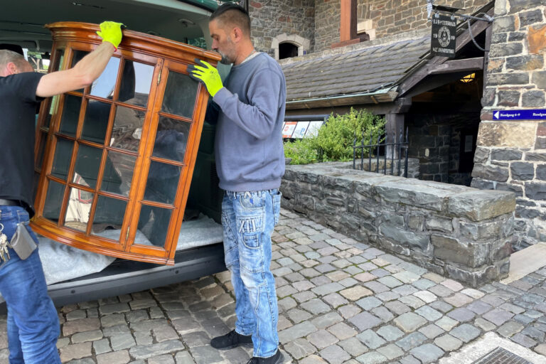 Die Museumstechniker der Burg Altena transportieren den Glasaufsatz eines Biedermeierschranks in die Räume der Sonderausstellung. Foto: Bernadette Lange Zwei Männer heben eine Vitrine aus einem Transporter