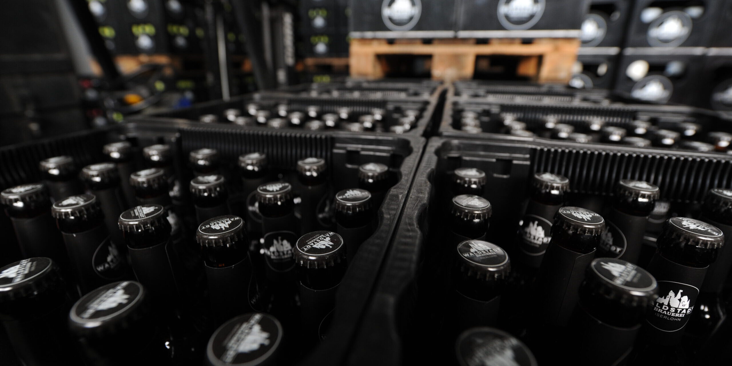 Auf Paletten stehen aufgereiht schwarze, gefüllte Bierkästen.