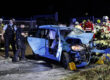Ein blauer Kleinwagen mit völlig eingedrückter Motorpartie steht auf einer Straße, umringt von Polizisten und Feuerwehrleuten.