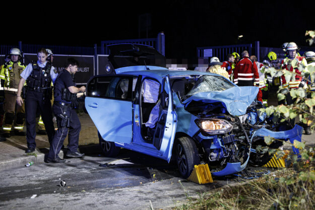 Foto: Dennis Echtermann Ein blauer Kleinwagen mit völlig eingedrückter Motorpartie steht auf einer Straße, umringt von Polizisten und Feuerwehrleuten.