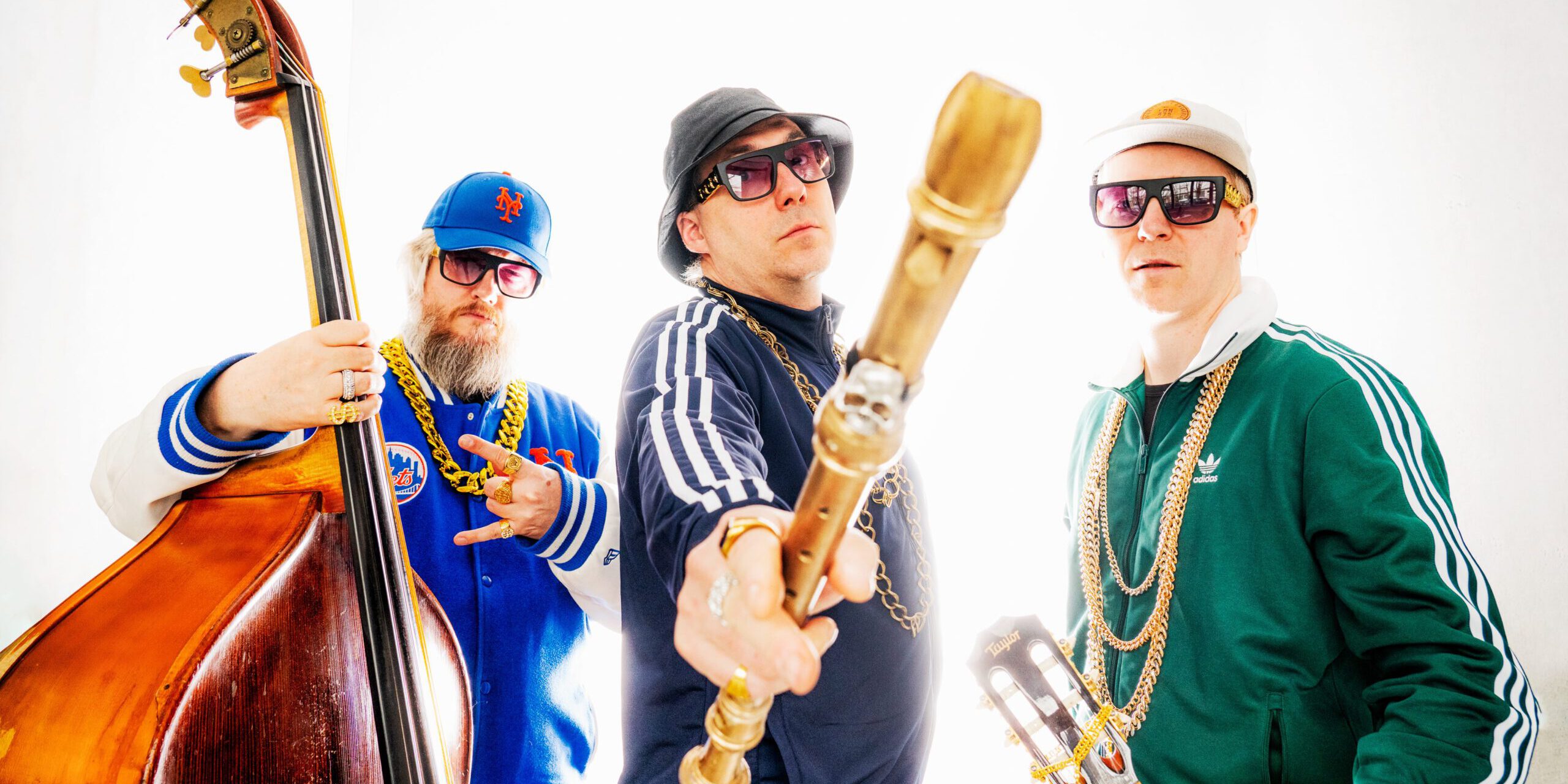 Drei Männer in Trainingsanzügen mit einem Kontrabass, einer Blockflöte und einer Gitarre