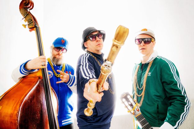 Drei Männer in Trainingsanzügen mit einem Kontrabass, einer Blockflöte und einer Gitarre