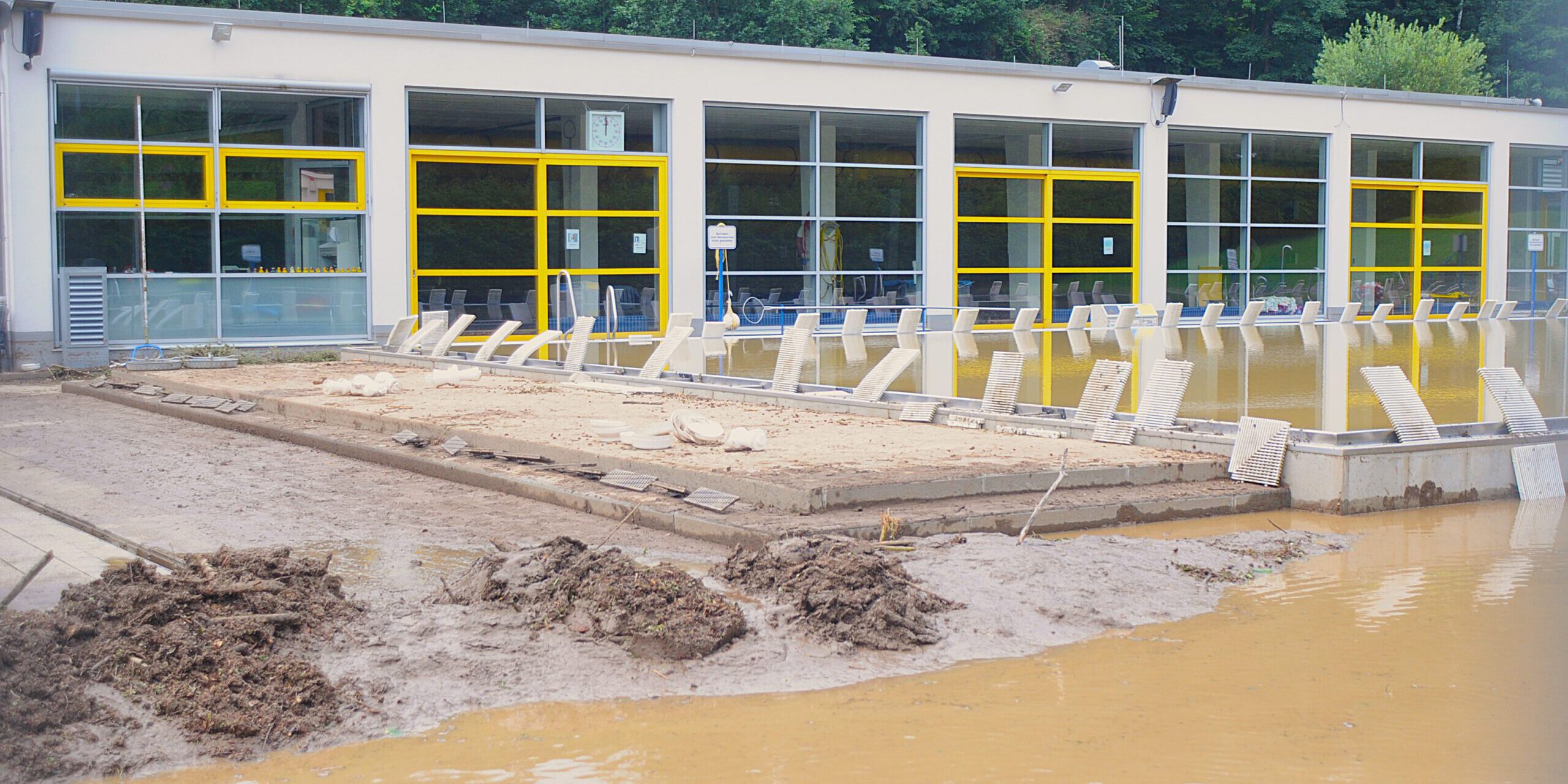 Das Außengelände und Schwimmbecken eines Freibads ist mit Schlamm und schmutzigem Wasser bedeckt.