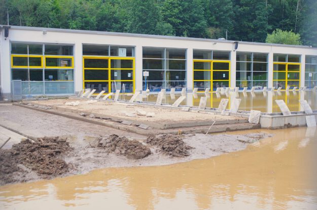 Foto: Carsten Menzel/Archiv Das Außengelände und Schwimmbecken eines Freibads ist mit Schlamm und schmutzigem Wasser bedeckt.