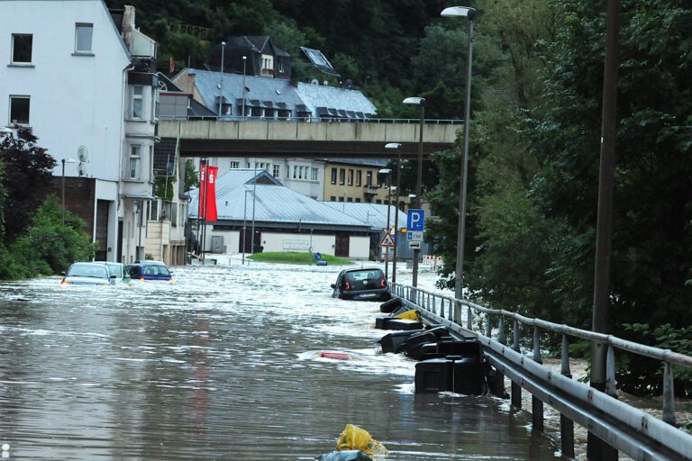 Foto: Carsten Menzel/Archiv Auf einer überschwemmten Uferstraße liegen oder dümpeln mehrere Autos und Mülltonnen.