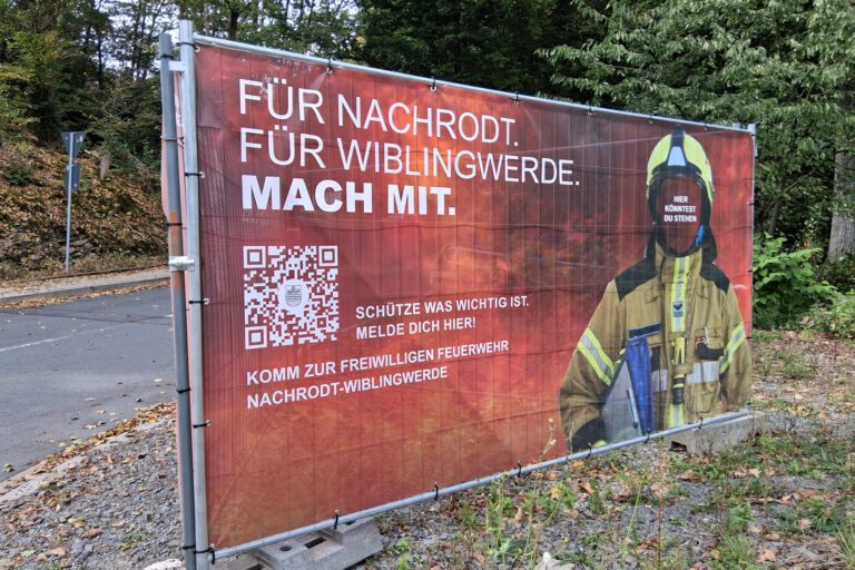 Ein Werbeschild der Feuerwehr steht an einer Straße.
