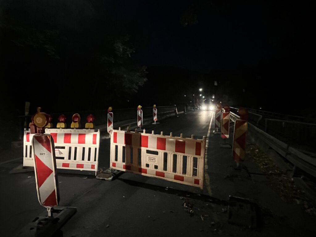 Rot-weiße Absperrbaken stehen auf einer Straße, die über eine Brücke führt.