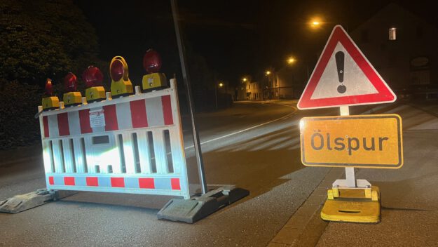 Foto: Carsten Menzel Rot-weiße Absperrbaken und ein Verkehrsschild "Achtung!" mit Zusatz "Ölspur" stehen auf einer nächtlichen Straße