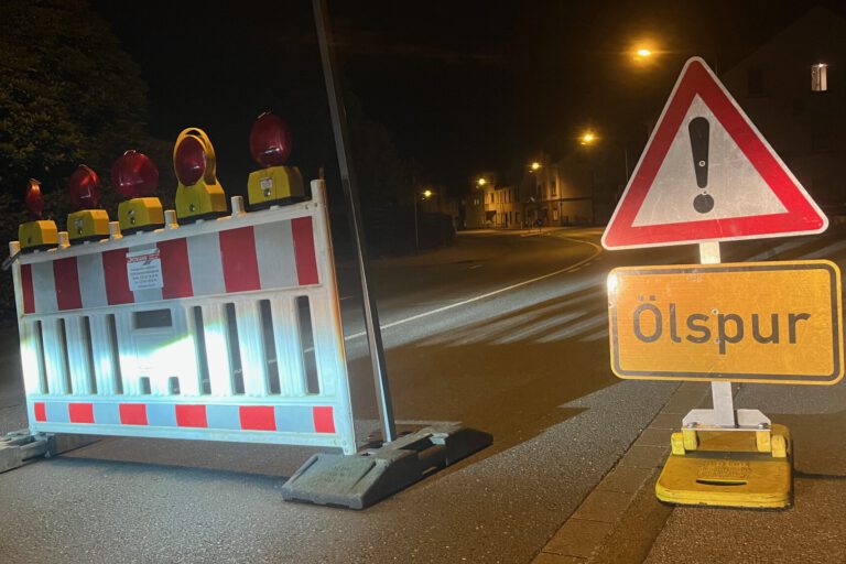 Foto: Carsten Menzel Rot-weiße Absperrbaken und ein Verkehrsschild "Achtung!" mit Zusatz "Ölspur" stehen auf einer nächtlichen Straße