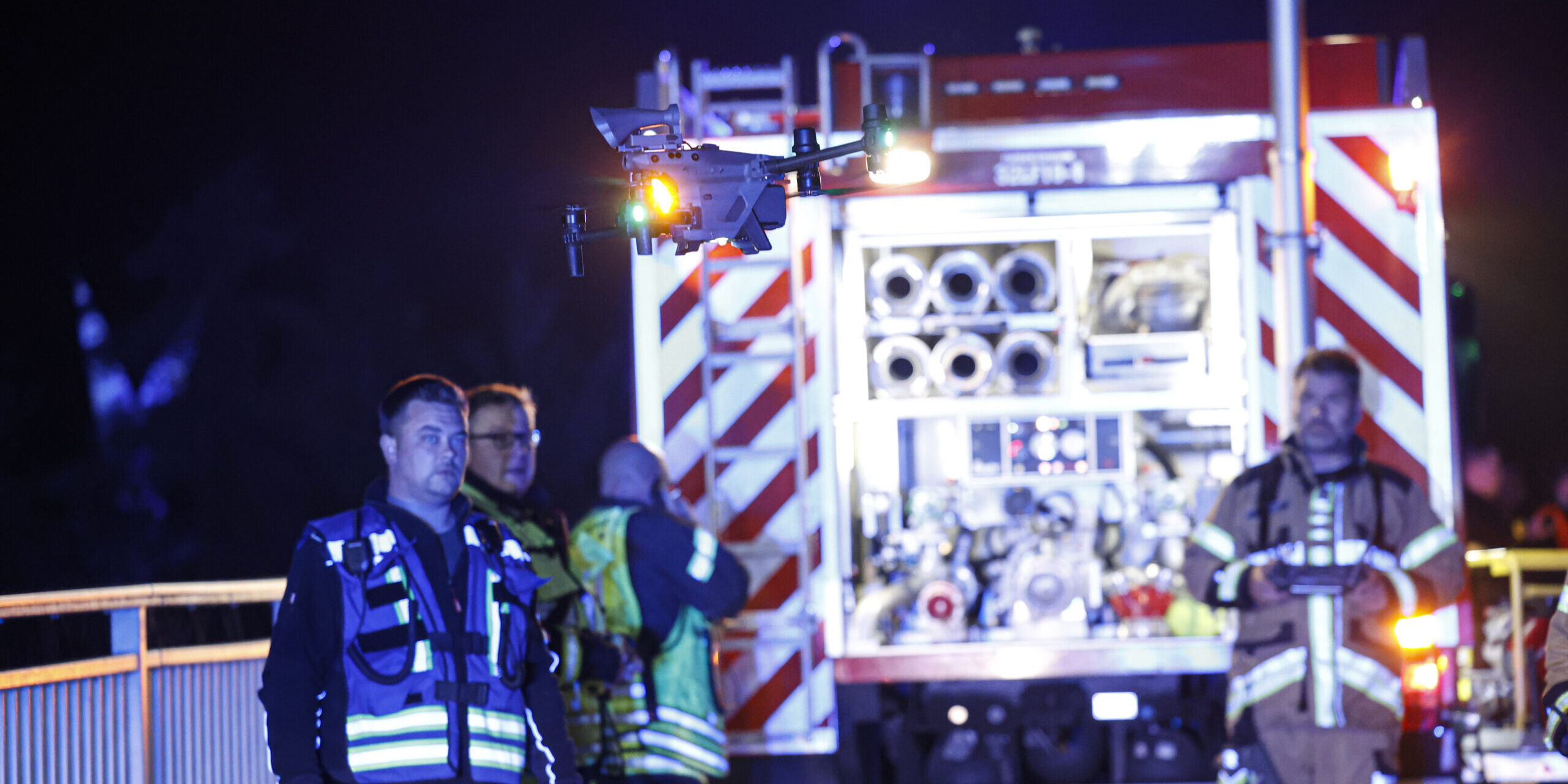 Feuerwehrleute stehen in der Nacht vor einem Feuerwehrwagen und lassen eine Drohne aufsteigen.
