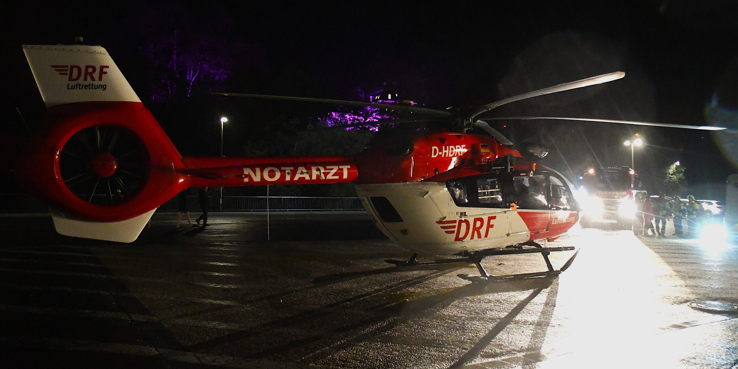 Ein rot-weißer Rettungshubschrauber der Luftrettung steht in der Dunkelheit auf einem Landeplatz auf einem Parkplatz.