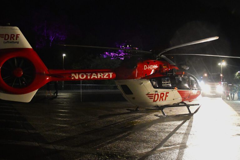 Ein rot-weißer Rettungshubschrauber der Luftrettung steht in der Dunkelheit auf einem Landeplatz auf einem Parkplatz.