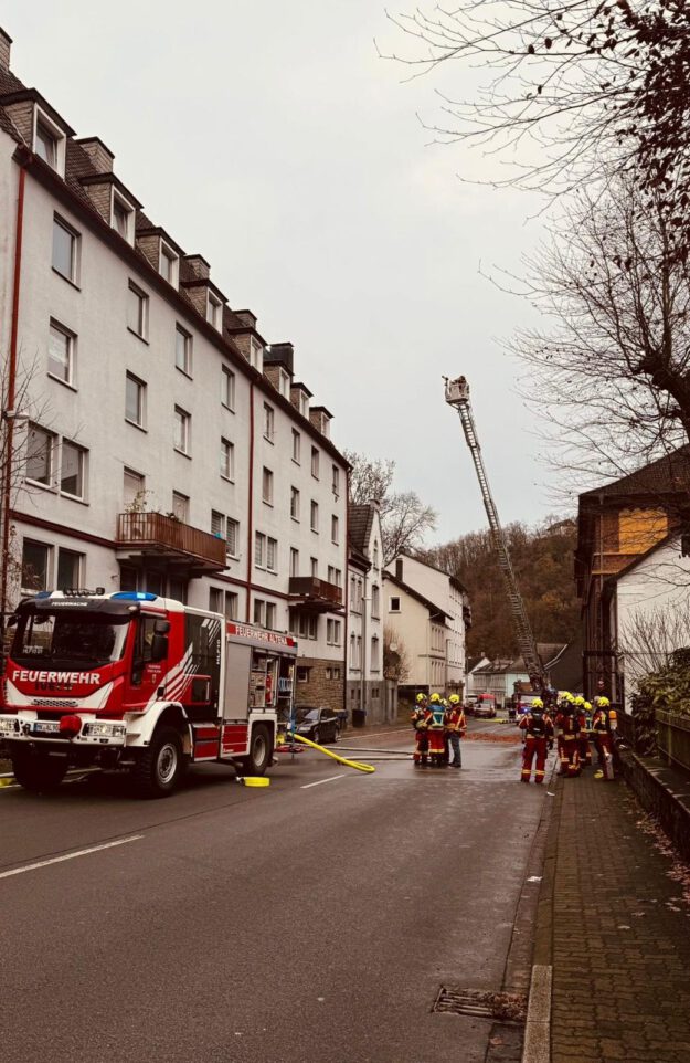 Foto: Rode/Rothämel/Feuerwehr Altena Ein Löschfahrzeug und eine ausgefahrene Drehleiter stehen auf einer Straße vor einem weiß angestrichenen Mehrfamilienhaus.