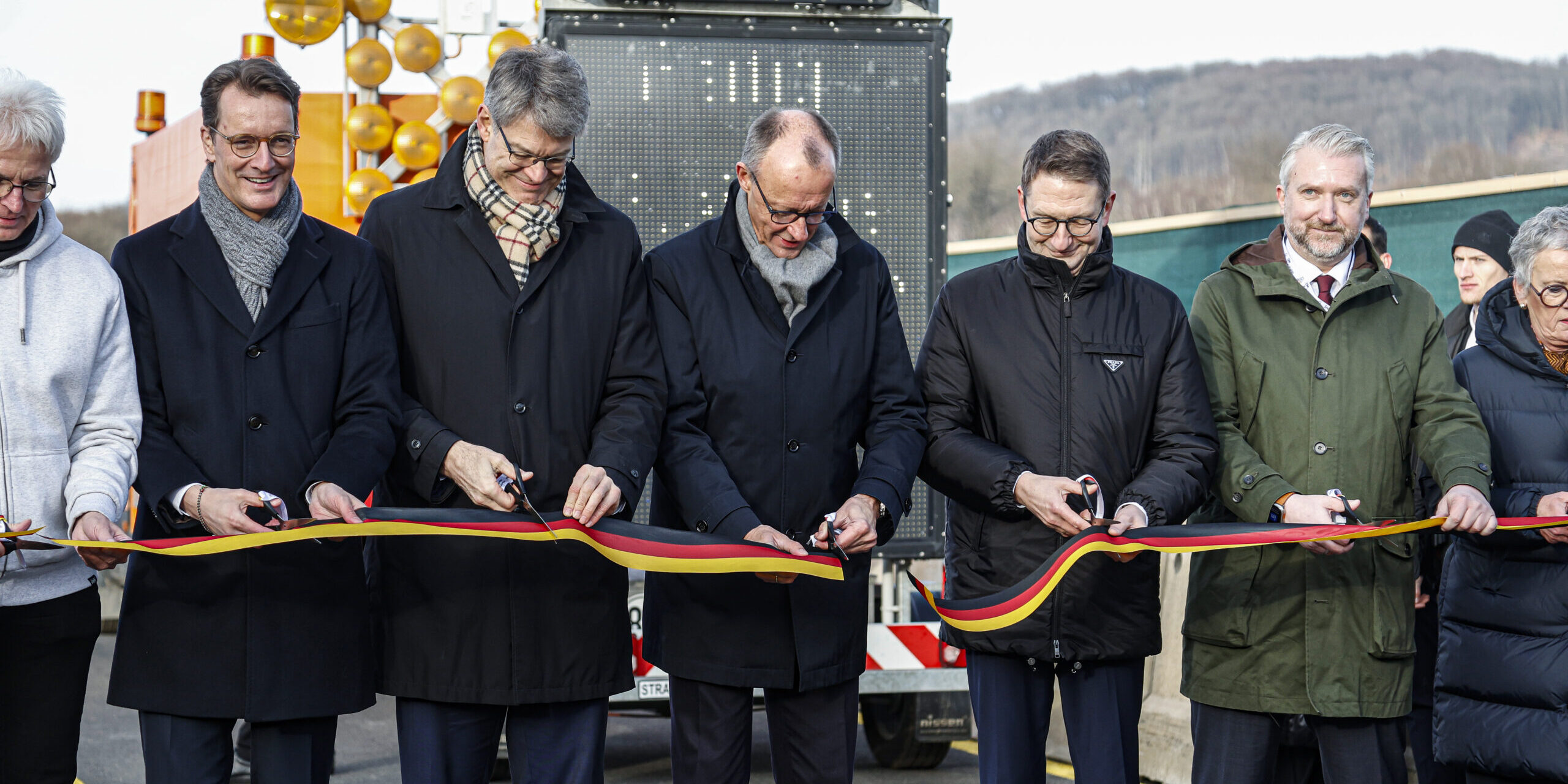 Fünf Männer, darunter Hendrik Wüst und Friedrich Merz, schneiden ein schwarz-rot-goldenes Band durch.
