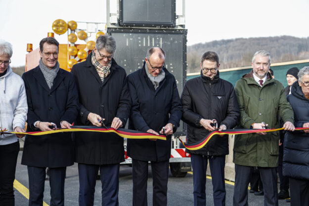 Fünf Männer, darunter Hendrik Wüst und Friedrich Merz, schneiden ein schwarz-rot-goldenes Band durch.