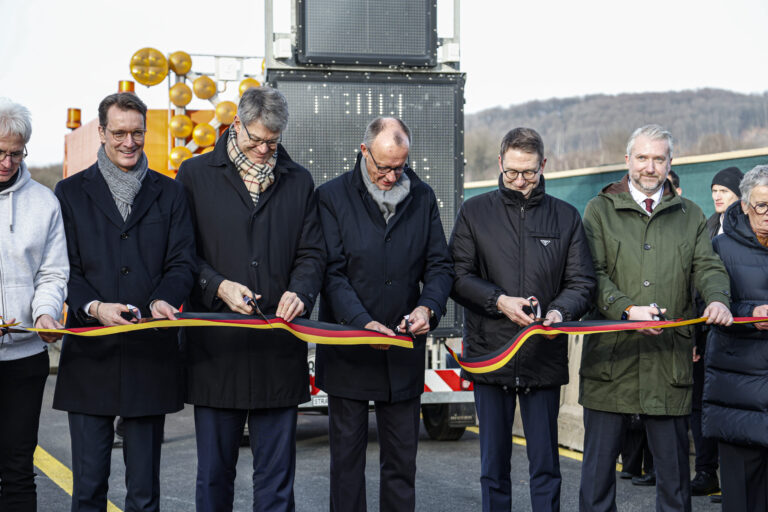 Fünf Männer, darunter Hendrik Wüst und Friedrich Merz, schneiden ein schwarz-rot-goldenes Band durch.