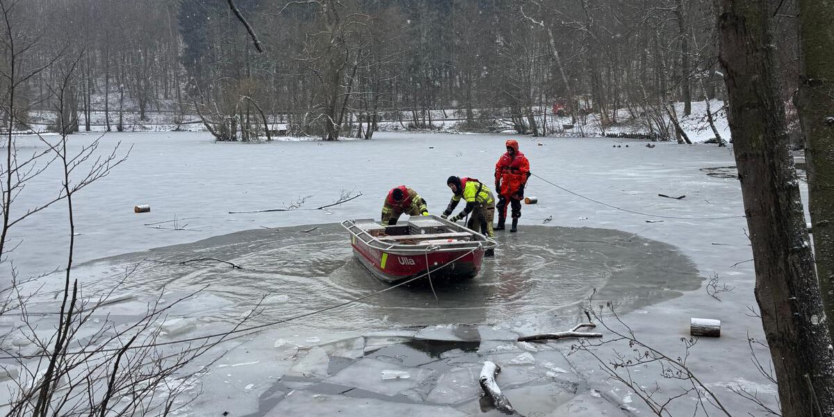Drei Feuerwehrleute mit einem Boot in einem Wasserloch eines ansonsten zugefrorenen Sees