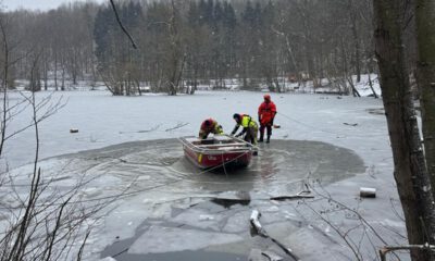 Drei Feuerwehrleute mit einem Boot in einem Wasserloch eines ansonsten zugefrorenen Sees